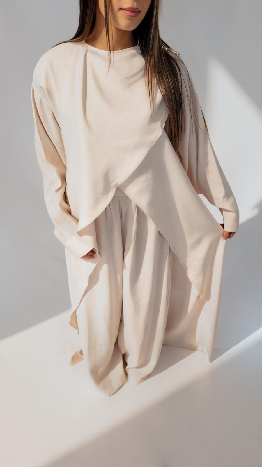 Ensemble drapé crème AZEL Paris porté de trois-quarts, broche dorée à l'épaule